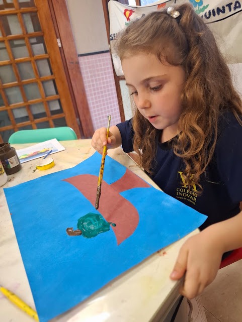 Criança da Educação Infantil criando pintura em sala preparada para atividades artísticas