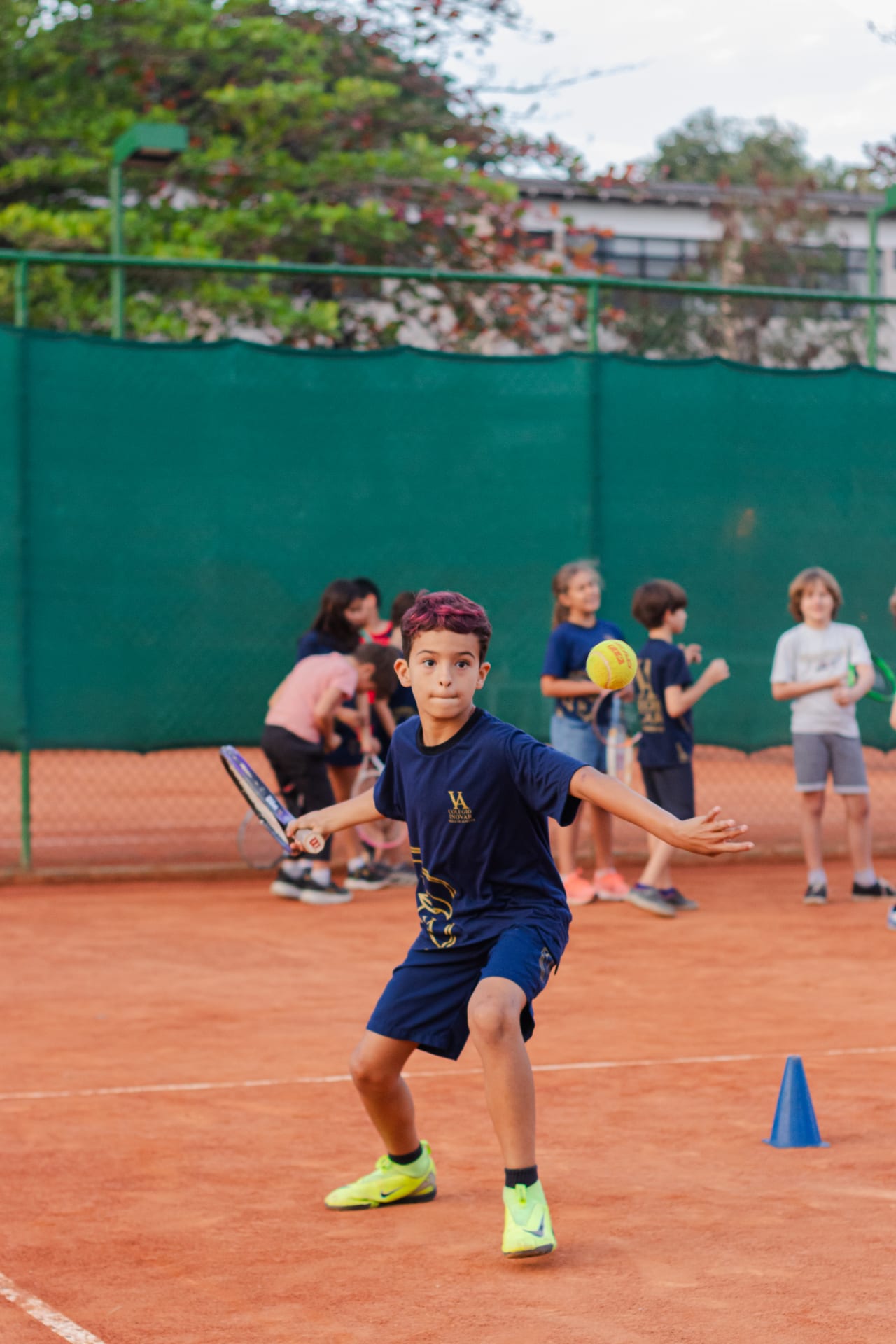 Aluno rebatendo a bola durante aula de tênis em quadra de saibro