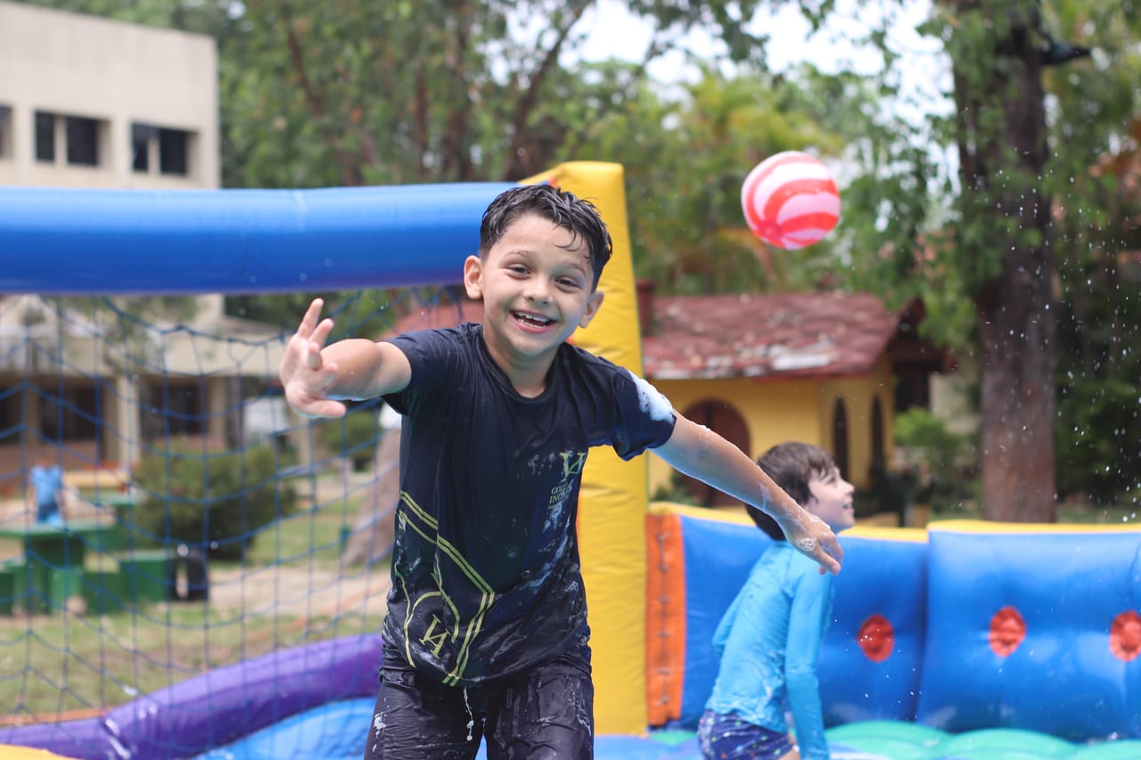 Aluno sorrindo e brincando com bola em um brinquedo inflável com água no Horário de Desenvolvimento Integral