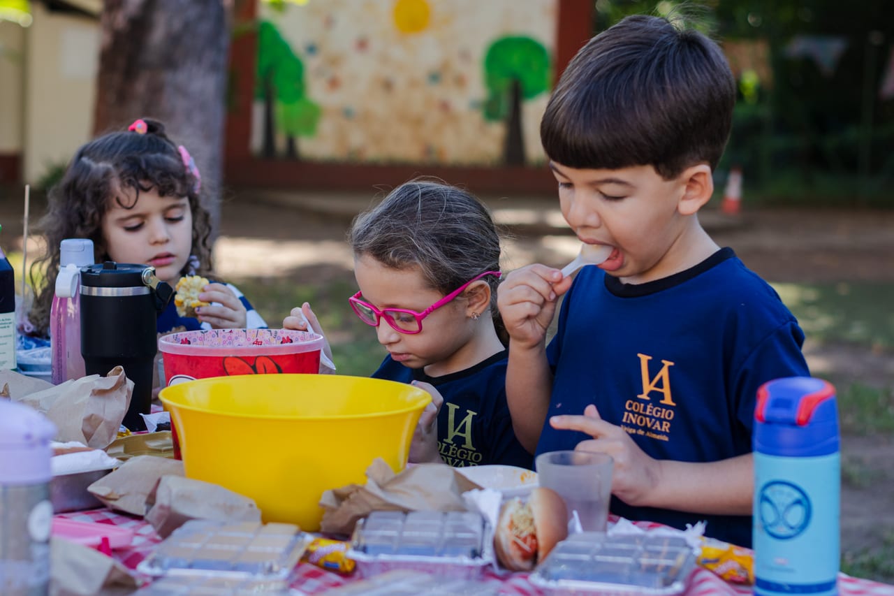 Crianças da Educação Infantil lanchando juntas em uma mesa ao ar livre