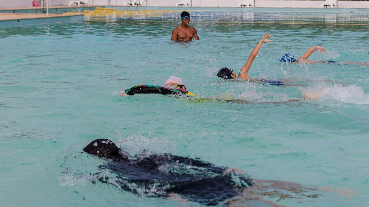 Estudantes nadando em raia durante aula de natação, com o professor dentro da piscina