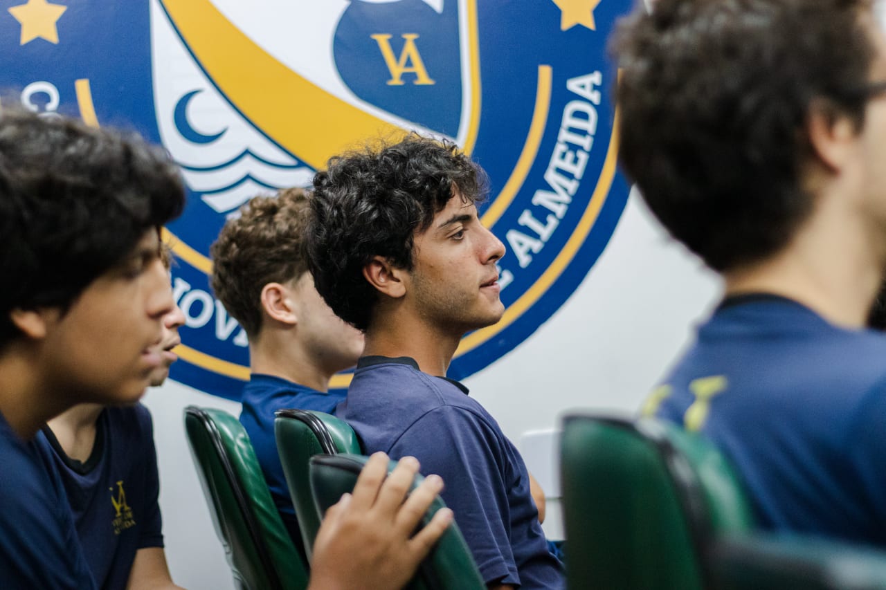 Alunos do Ensino Médio atentos a uma apresentação diante do brasão do Colégio Inovar Veiga de Almeida